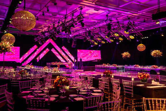 Salón de gala con iluminación magenta, trusses, pantallas LED y esferas doradas suspendidas — iluminación Stöessel